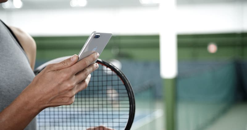 Person looking at their phone while holding a tennis racquet